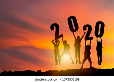 New Year Sillhouette Concept. Celebrating The Transition From The Old Year To The New Year. A Group Of Friends Hold Signs, Numbers 2020, Jump Happy.