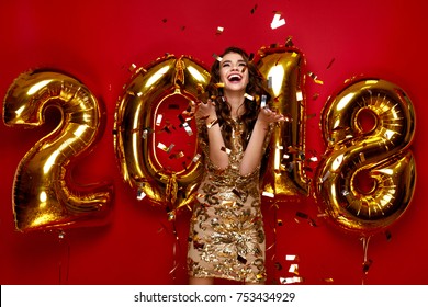 New Year. Woman With Balloons Celebrating At Party. Portrait Of Beautiful Smiling Girl In Shiny Golden Dress Throwing Confetti, Having Fun With Gold 2018 Balloons On Background. High Resolution.