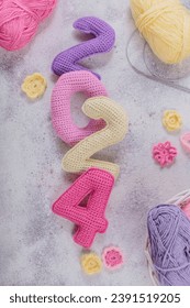 New Years background 2024. Multicolored crochet numbers, skein of wool yarn and knitting needles on gray background. New Years start creative handcrafted idea for DIY crafters