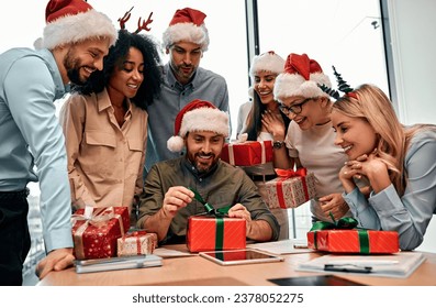 New Year's and Christmas mood. Group of business people in Santa hats, colleagues unpacking gifts at work in the office. - Powered by Shutterstock