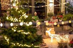 New Year's Decorated Backyard With Woman Sitting On Background At Night. Woman Enjoying Winter Holidays At Home Alone