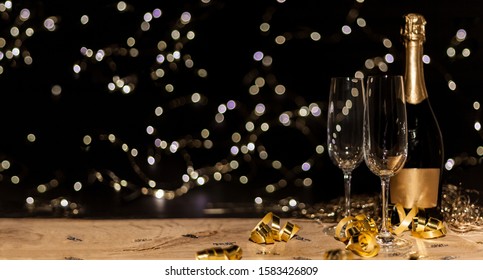 New Year's Eve Background With Champagne Bottle And Glasses Confetti And Gold Snakes New Year's Eve Background With Confetti And Gold Snakes On Wooden Table, Lights