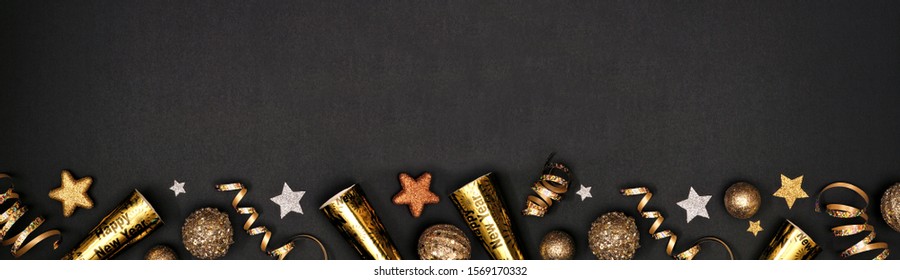 New Years Eve border banner of glittery gold stars, streamers, decorations and noisemakers. Above view over a black background.