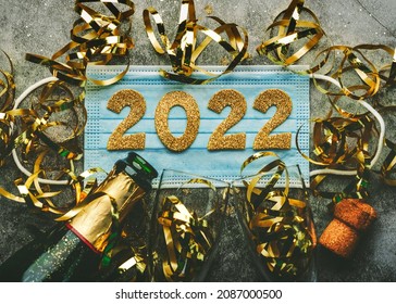 New Years Eve Celebration Concept Background.Medical Mask With The Numbers 2022 And Champagne Bottle With Glasses On Gray Background .Covid-19 New Year Concept On Gray Background