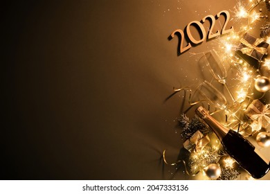 New Years Eve holiday background with fir branches, number 2022, champagne bottle, christmas balls, gift box and lights on dark board - Powered by Shutterstock