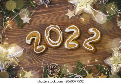 New Year's flatlay with ginger cookies in the form of numbers 2022 with Christmas tree branches, cones and decorations, with a bokeh light garland. On a white wooden background