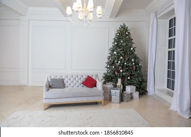 New Year's Interior With Fir Tree In Bright Tones Near Window. Christmas White Living Room Interior With Vintage Gray Sofa, Gifts In Silver Packaging And Christmas Tree. Location For Photo Shoot.