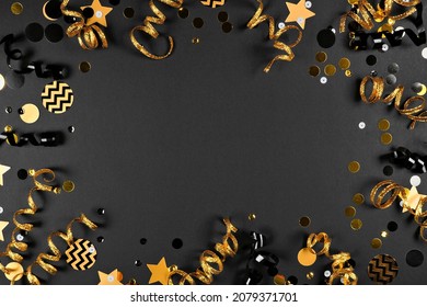 New Years Party Frame Of Shiny Black And Gold Black And Gold Streamers And Confetti. Top Down View On A Black Background.