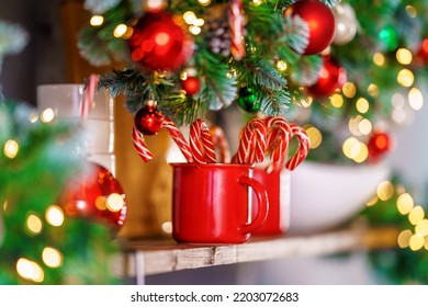 New Year's red cup with candy canes, stands on kitchen shelf, festive lighting bokeh, on background kitchen, decorated for holiday. Christmas interior with blurry background.
