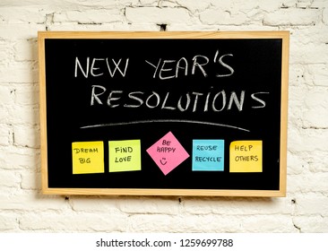 New Year's Resolution Written On Blackboard With Colorful Notes Of Dreams Wishes And Trendy Lettering Post Its For Happy Life Goals And Self Management Concept Hanging On White Brick Wall Background.