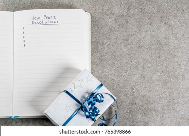 New Years Resolutions Concept, Open Notebook On A Grey Stone Table Table. With Christmas Gift And Blank List. Copy Space