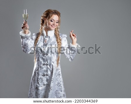 New Year's toast, a young beautiful blonde in a Snow maiden costume clinks a glass of champagne, photo on gray, copy space