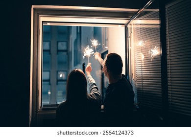 New Year's window sparkler firework. Couple celebrating at home. Eve party with family. Sparkle in the night. Happy people on Christmas. Silhouette of two people holding light. Man and woman in love. - Powered by Shutterstock