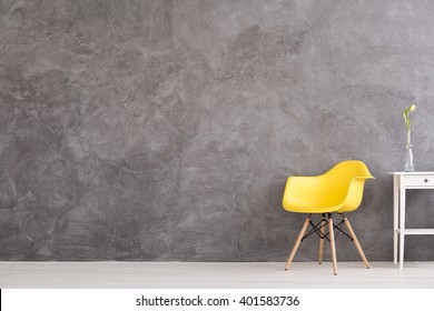 New Yellow Chair And Small, Decorative Table Standing In Interior With Grey Wall