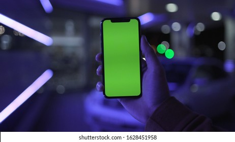 NEW YORK - April 19, 2019: Night light young man hands holding use smartphone with vertical green screen on night city colorful background white car communication device hands digital gadget phone