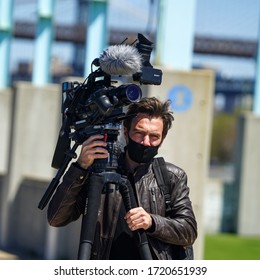 NEW YORK - APRIL 28, 2020: Cameraman Wears Face Mask  During Coronavirus Pandemic At Brooklyn Bridge Park In New York