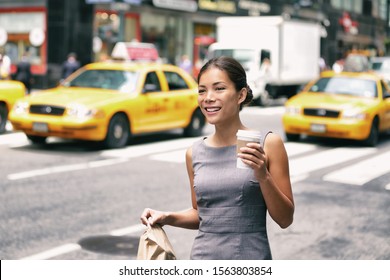 New York Asian Business Woman Walking To Work With Lunch Bag In The Morning Commuting Drinking Coffee Cup On Street With Yellow Cabs In The Background. People Commuter Lifestyle.