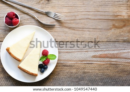 New York cheesecake or classic cheesecake with fresh berries on white plate, wooden table background and copy space for text