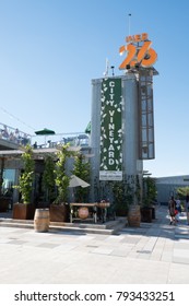 New York City - 3 June 2017: People Walking Passed The Entrance To City Vineyard, A Trendy New York Rooftop Bar In Lower Manhattan At Pier 26 On A Summer Day, Blue Sky With No Clouds.