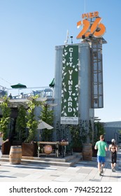 New York City - 3 June 2017: Man And Woman Walking Passed City Vineyard, A Trendy New York Rooftop Bar In Lower Manhattan At Pier 26 On A Summer Day, Blue Sky With No Clouds. 