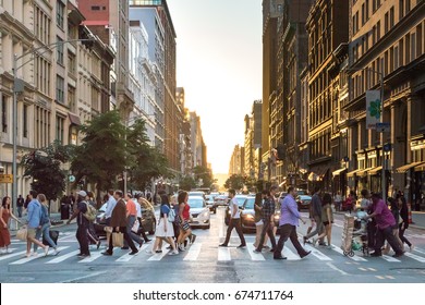 NEW YORK CITY - CIRCA 2017: Busy crowds of people cross the intersection of 5th Avenue and 23rd Street in Manhattan, New York City with the colorful setting sun in the background on June 3rd, 2017.