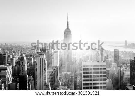 New York City. Manhattan downtown skyline with illuminated Empire State Building and skyscrapers at sunset. Vertical composition. Sunbeams and lens flare. Black and white image.