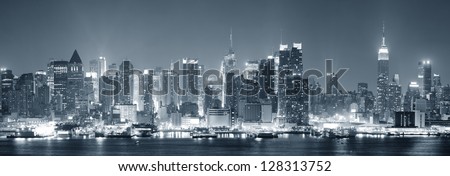 New York City Manhattan midtown skyline black and white at night with skyscrapers lit over Hudson River with reflections.
