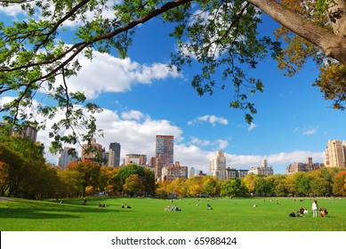 New York City Manhattan Skyline Panorama Viewed From Central Park With Cloud And Blue Sky And People In Lawn.