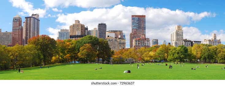 New York City Manhattan Skyline Panorama Viewed From Central Park With Cloud And Blue Sky And People In Lawn.