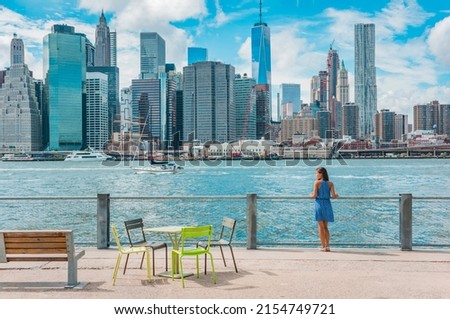 New York city Manhattan skyline seen from Brooklyn waterfront - woman enjoying view. American people walking enjoying view of Manhattan over the Hudson river from the Brooklyn side. NYC cityscape