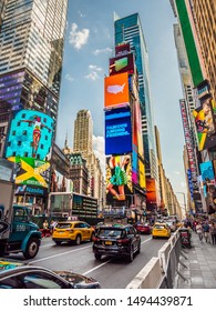 New York City, New York - May 19th, 2017: Traffic Makes Its Way Through The Bustling Busy Streets In The Center Of Times Square As People Pass By On The Sidewalk Protected By Concrete Barricades.