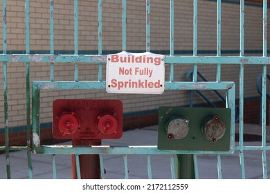 New York City, NY United States - June 26, 2022: White sign on fence reads "Building Not Fully Sprinkled" above fire sprinkler system on metal fence in Washington Heights, Manhattan on summer day