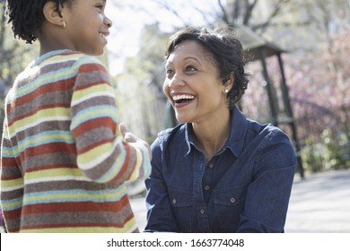 A New York City, Park In The Spring. Sunshine And Cherry Blossom. A Mother Kneeling Down Smiling At Her Son.