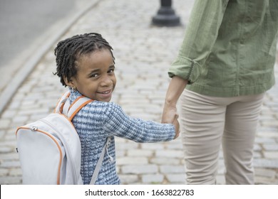 A New York City, Park In The Spring. Sunshine And Cherry Blossom. A Boy Wearing A School Bookbag, And Walking Hand In Hand With A Woman.