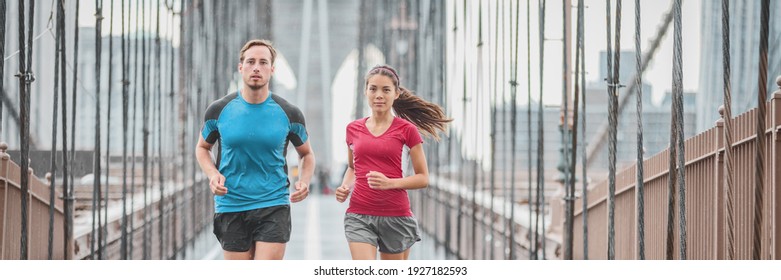 New York city runners athletes training for run marathon on Brooklyn Bridge banner. Fit active interracial couple on outdoor running exercise in raining day. Summer rain. Asian woman, Caucasian man.