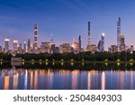 New York City skyline at dusk with reflections of Billionaires Row supertall skyscrapers in Central Park Reservoir. Evening view of illuminated luxury towers in Midtown Manhattan