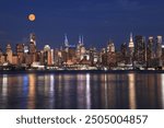 New York City skyline illuminated at dusk with orange full moon, view from Hudson River, USA