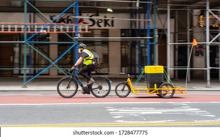 New York City, USA - 5/5/2020:  Bicycle Delivery Man Riding On 23rd Street During The Coronavirus Pandemic. Bike Trailer With Bins Used To Deliver Of Packages And Produce To Costumers Homes In NYC.