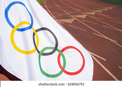 NEW YORK CITY, USA - AUGUST 30, 2015: Olympic Flag Waves Across The Lanes Of A Traditional Red Tartan Running Track.