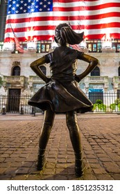 NEW YORK CITY, USA - MARCH 15, 2020:  Fearless Girl Statue Looking Up At  New York Stock Exchange Building At Wall Street In Manhattan At Night, New York City, USA