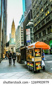 New York City, New York / USA – May 2017: Couple Walking On NYC Street With Hot Dog Cart In Foreground And Empire State Building In Background