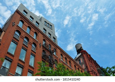 New York City, USA-June 2020; Low angle view of part of the facade of a red brick building with modern top floor (NYU Wagner); water tower on the right roof top