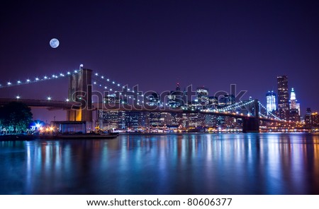 New York City's Brooklyn Bridge and Manhattan skyline illuminated at night with a full moon overhead.