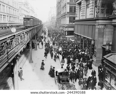 New York City's Sixth Avenue crowded with shoppers in 1903. Horse drawn carriages and wagons travel on the street level as an elevated train passes above.