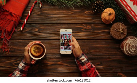 NEW YORK - January 08, 2017: Social Media. Instagram App. Woman Scrolling Photos And Putting Like On The Christmas Dog Picture. Christmas Atmosphere On The Brown Table. Flat Lay.