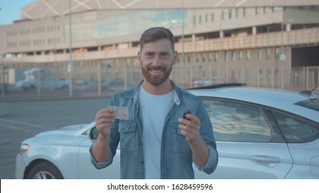 NEW YORK - June 10, 2018: Portrait Of Cheerful Handsome Man Showing His Driver License And Key Standing By New Modern Car In The City. Happy Driver Beginner. Celebration.