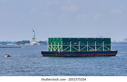 New York, NY - August 26, 2021: A barge loaded with municipal-waste shipping containers moored in NY Harbor in front of The Statue of Liberty on a hot summer day. 