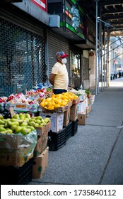 New York, NY / United States - May 16th 2020: A man wears a mask while selling fruit on the streets of Washington Heights, Manhattan, New York City during the COVID-19 pandemic. 