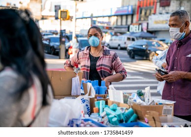 New York, NY / United States - May 16th 2020: A woman wearing a mask sells beauty products at a street stall in Washington Heights, Manhattan, New York City during the COVID-19 pandemic. 