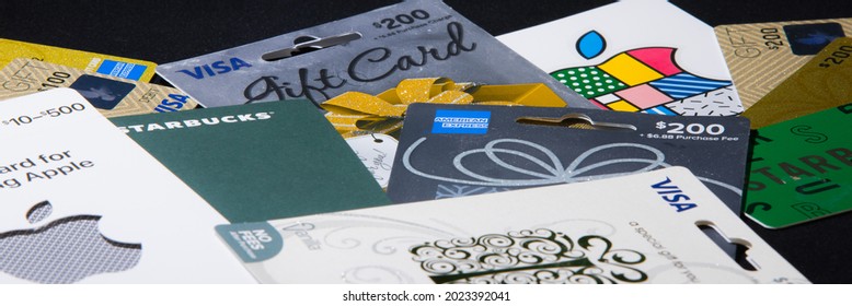 New York, NY, USA 8-9-2021: Variety of gift cards and matching envelope cases placed flat on a plain black background. Multiple card issuers and merchants. Low diagonal angle. Header crop.